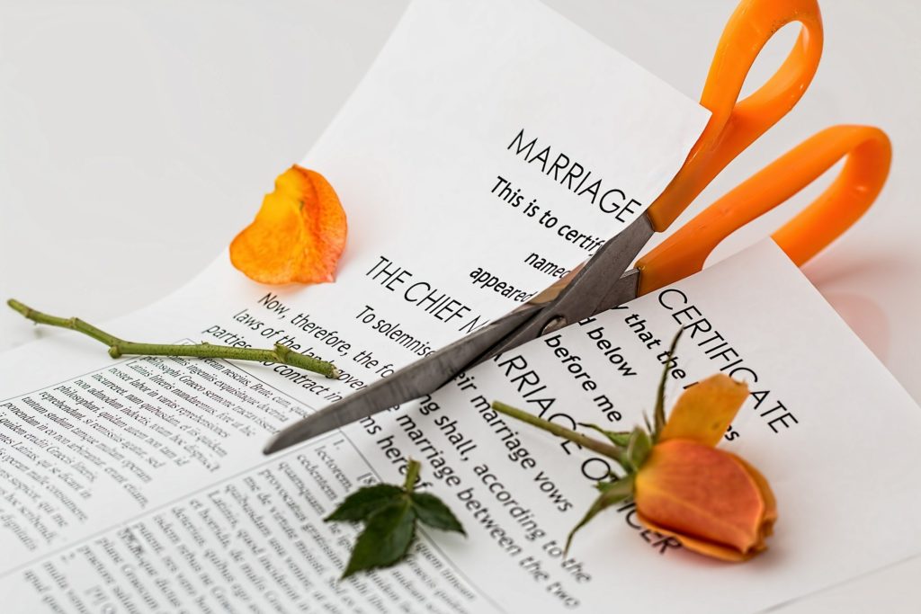 Eine Schere, die eine Heiratsurkunde sowie eine gelbe Rose durchschneidet.